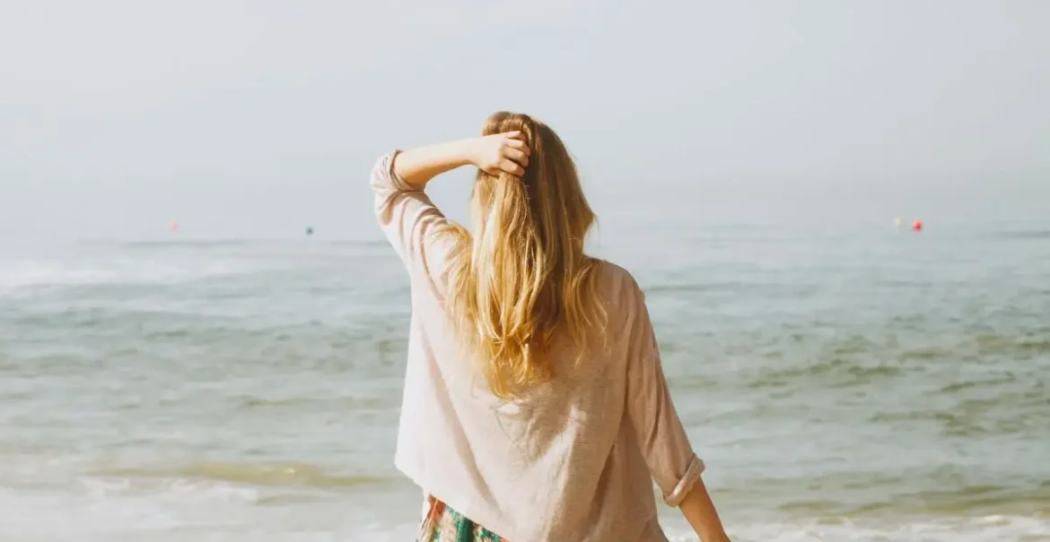 Cover image for the benefits of minimalism blog which shows a woman looking out at a calm ocean with a hand on her head