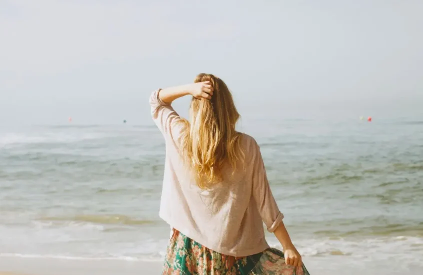 Cover image for the benefits of minimalism blog which shows a woman looking out at a calm ocean with a hand on her head