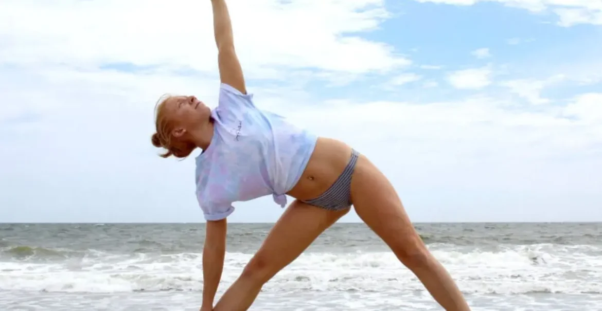 Cover image for the best yoga poses for flexibility blog, which shows a woman doing triangle pose in front of the ocean