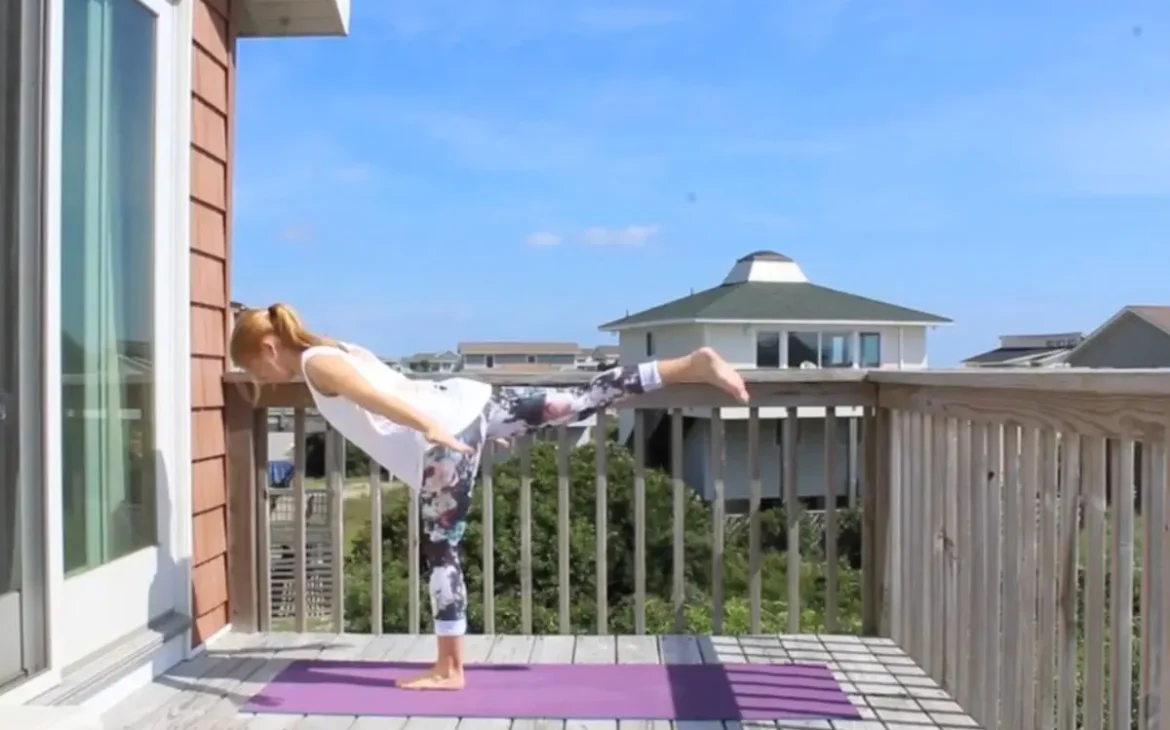 Young redhead woman doing airplane yoga pose on a yoga mat on a sunny deck