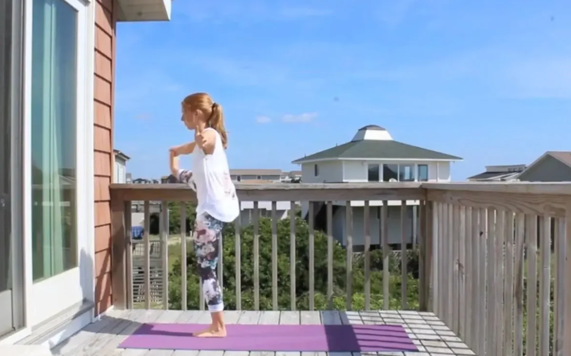 Young redhead woman doing hand to toe yoga pose on a yoga mat on a sunny deck