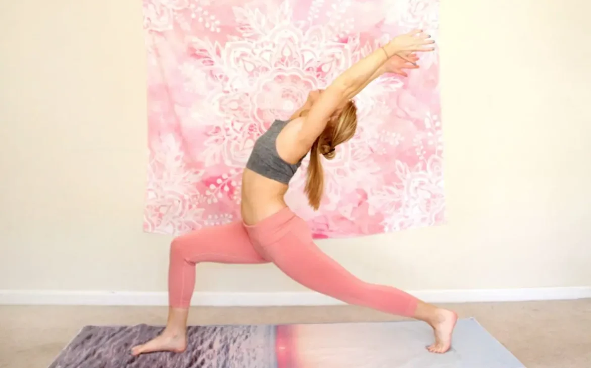 Young redhead woman doing the heart opening yoga pose, warrior one, on a yoga mat indoors
