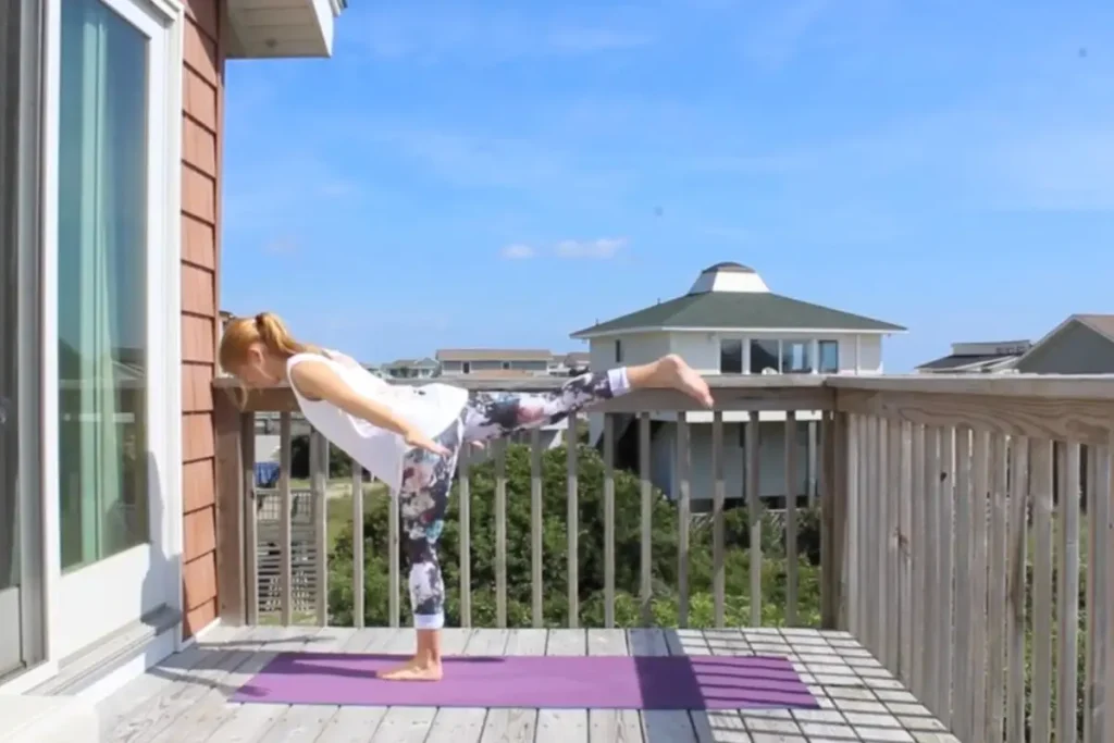 Redhead woman doing the airplane yoga pose on a sunny deck
