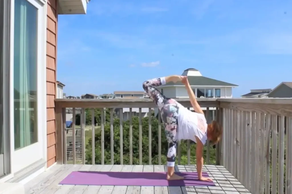 Redhead woman doing the bound half moon pose on a sunny deck