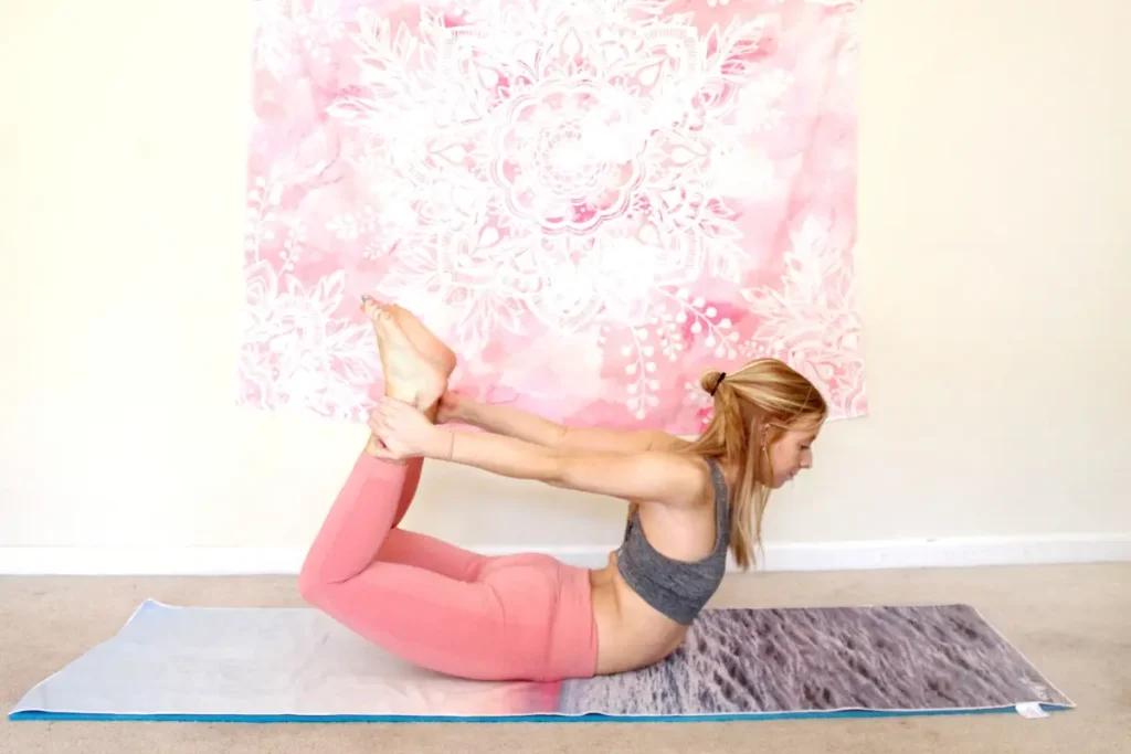 Redhead woman doing the heart opening yoga pose, bow pose, on a yoga mat indoors