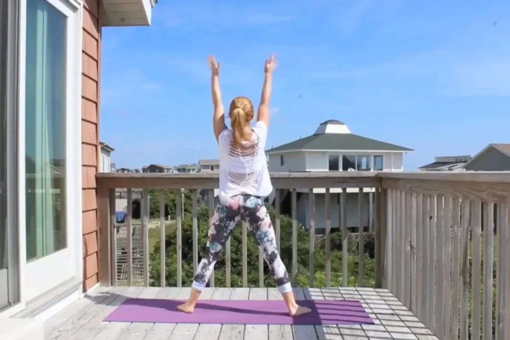 Redhead woman doing the buddha squats yoga pose, reaching up in the air, on a sunny deck
