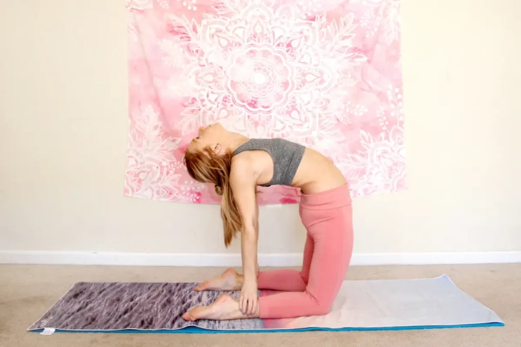 Young redhead woman doing the heart opening yoga pose, camel pose, on a yoga mat indoors