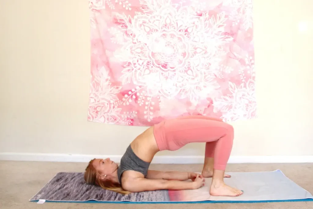 Young redhead woman doing the heart opening yoga pose, bridge pose, on a yoga mat indoors