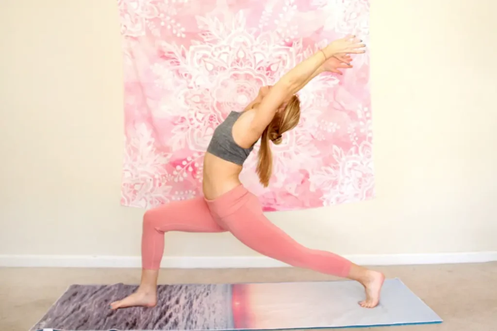 Young redhead woman doing the heart opening yoga pose, warrior one, on a yoga mat indoors