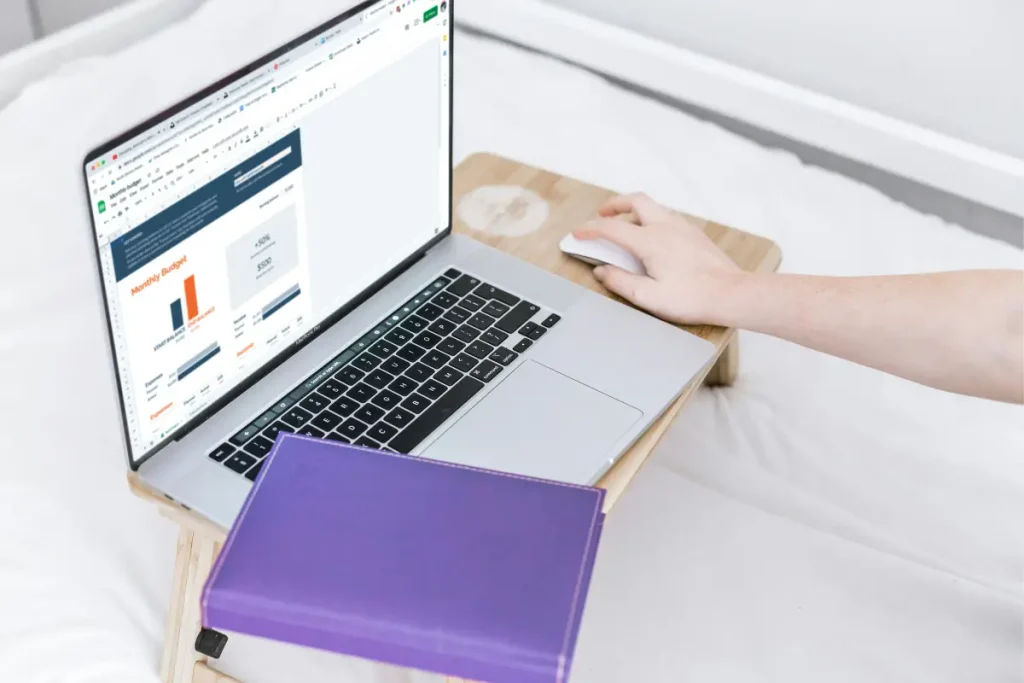 Person working on the computer to look at a budgeting tool with a notebook, to clear their money blocks
