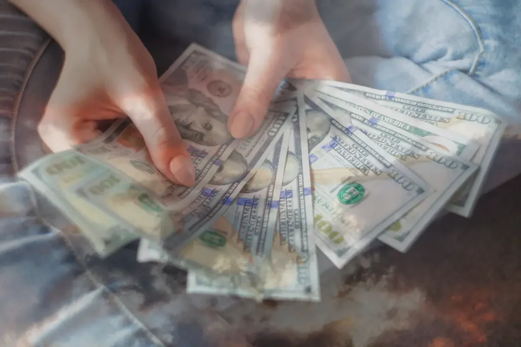 A woman holding a bunch of $100 bills, to demonstrate the importance of removing money blocks for more abundance