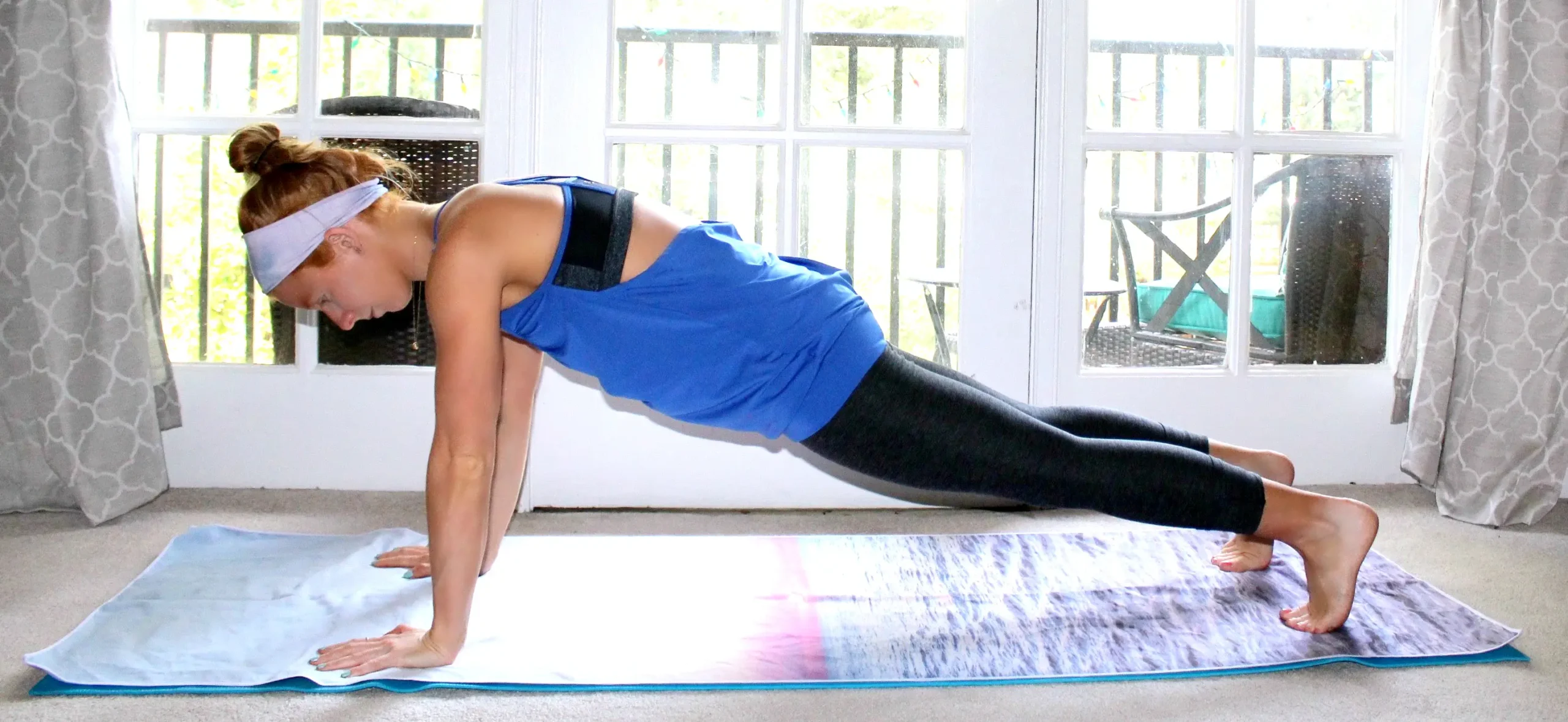 Small redhead woman doing the plank yoga pose on a colorful yoga mat