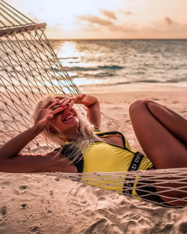 Woman laying on a hammock with her hands over her eyes smiling as the sun sets