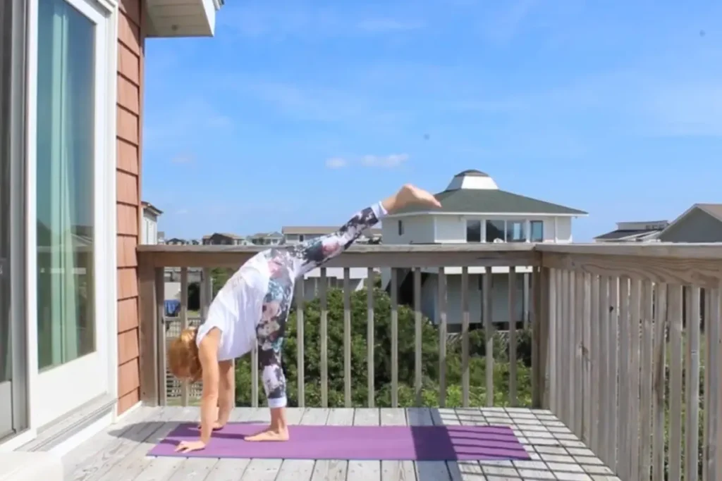 Redhead woman doing the standing split yoga pose on a sunny deck