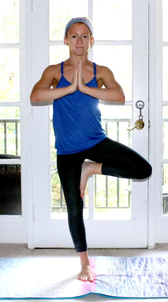Small redhead woman doing the tree yoga pose on a colorful yoga mat