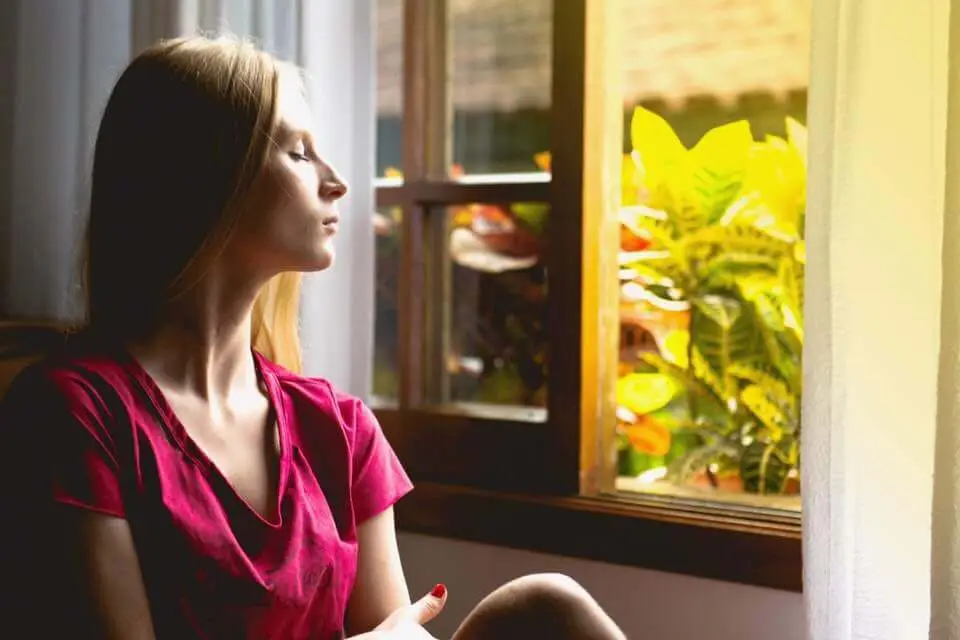 woman looking out window at peace Blonde woman sitting with her eyes shut looking out the window with sun shining outside