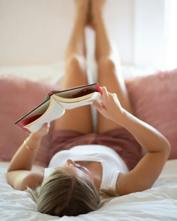 Woman laying on her bed holding up a book relaxing